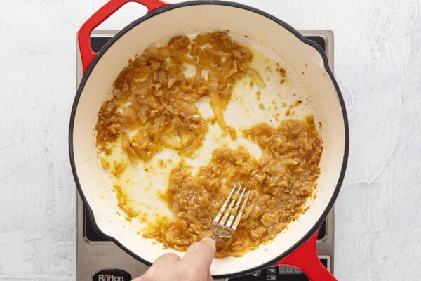 A person mashing caramelized onion and garlic together in a skillet.