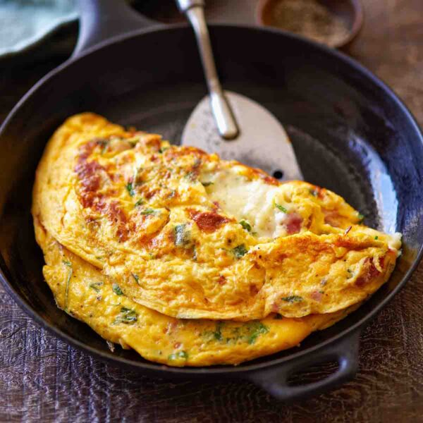 A cooked ham and cheese omelet in a small skillet with a spatula sliding underneath to flip it.