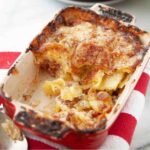 A ham, cheese, and potato casserole in a large rectangular dish, on a red-and-white striped towel.