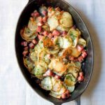 A Dutch oven filled with ham and potatoes sarladaise on a white and red linen cloth.
