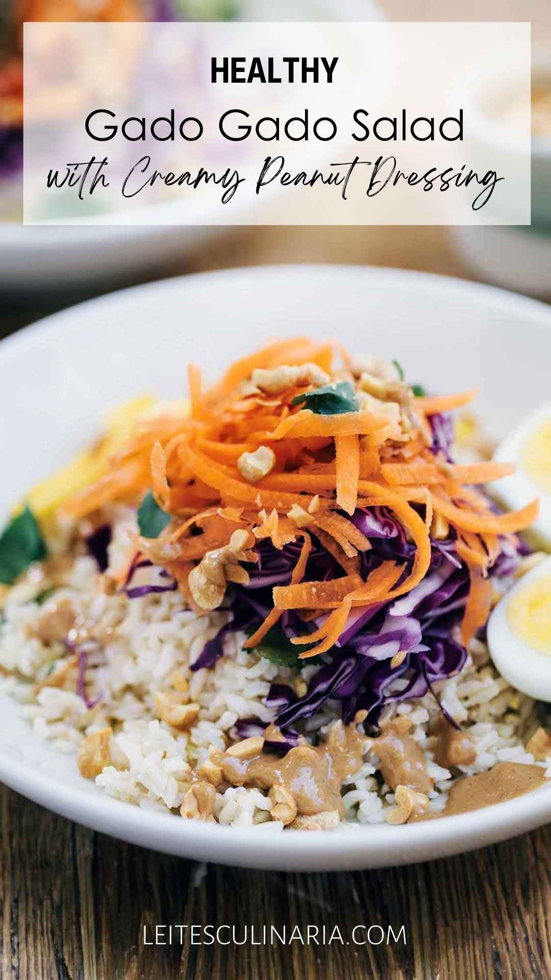 A white bowl filled with gado gado salad with rice, cabbage, carrots, peanuts, egg, and creamy peanut dressing.