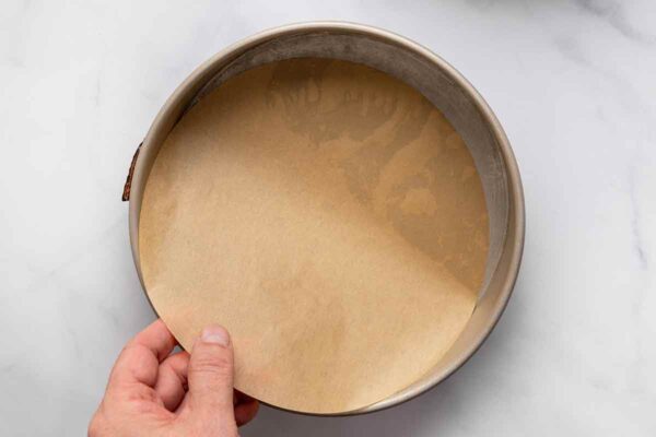 A person lining a cake pan with parchment paper.
