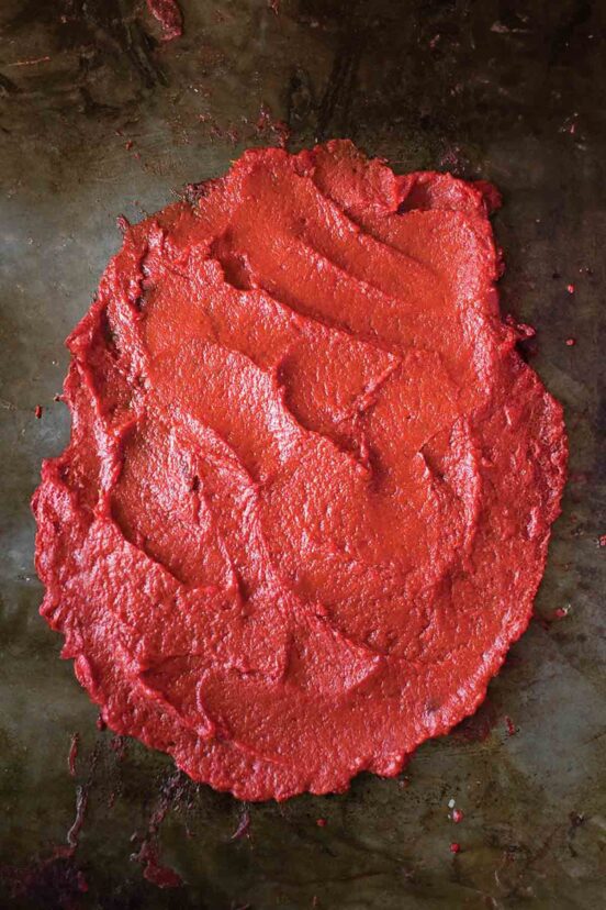 A metal sheet pan covered with spread-out tomato paste.