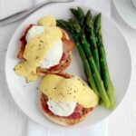 Two Julia Child's eggs Benedict on a white plate with a side of asparagus.
