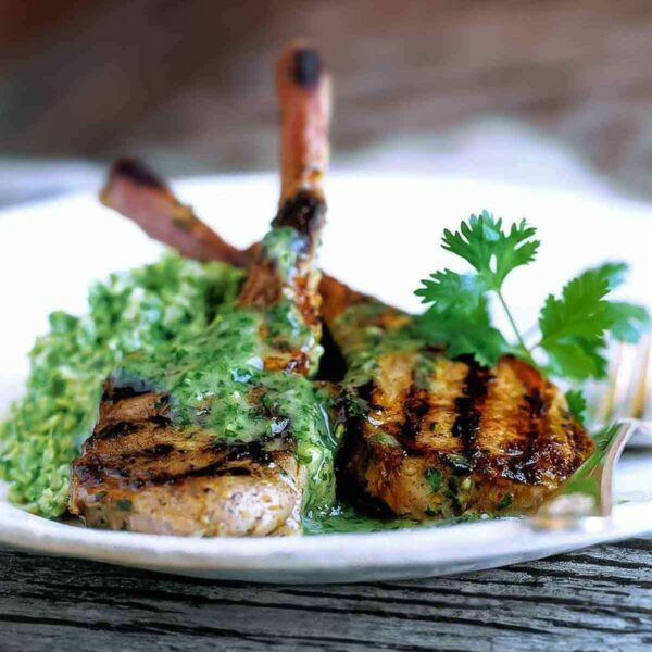 Two grilled lamb chops topped with cilantro-mint sauce on a white plate.