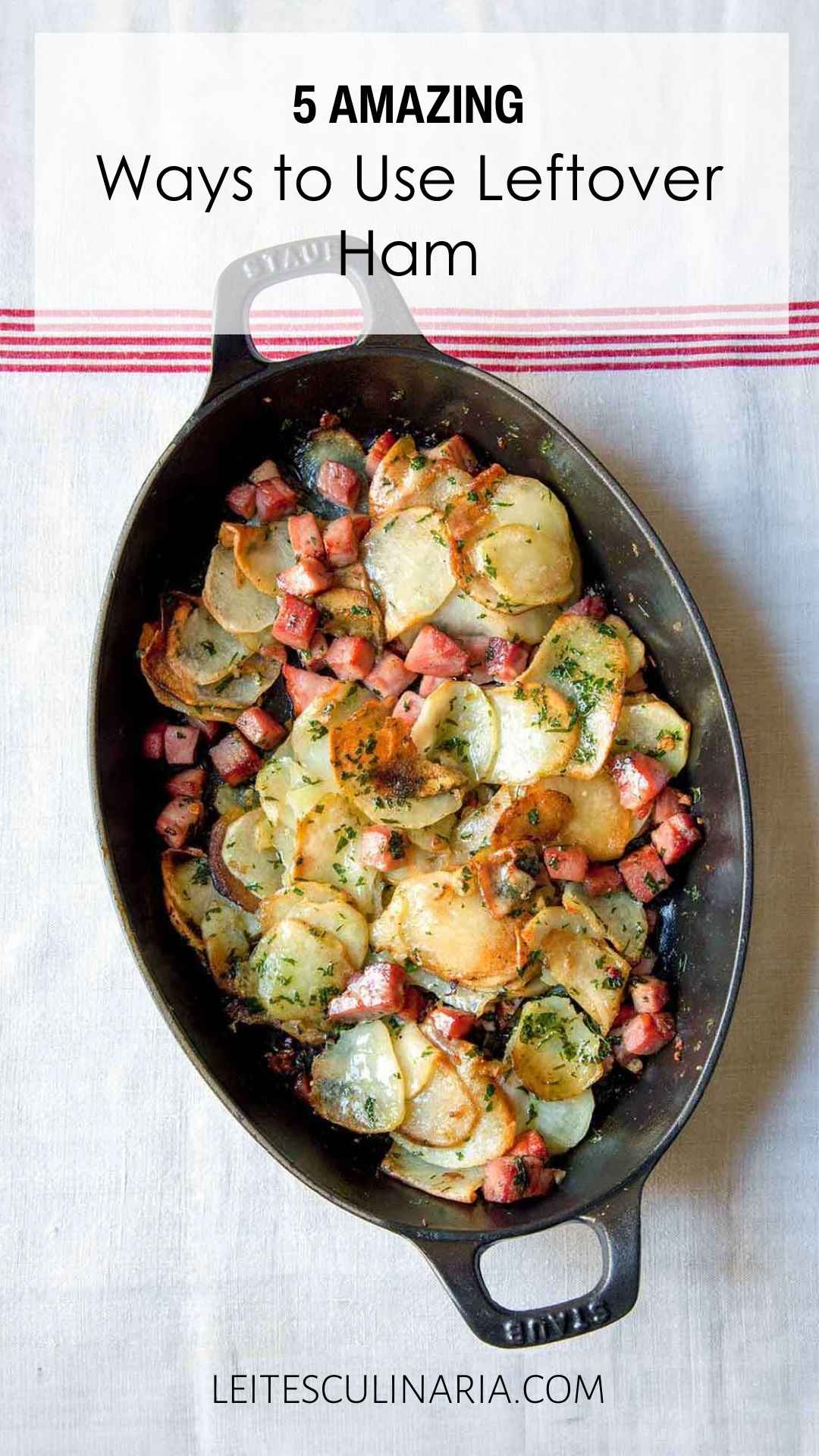 An oval baking dish filled with sliced potatoes, cubed ham, and chopped herbs.
