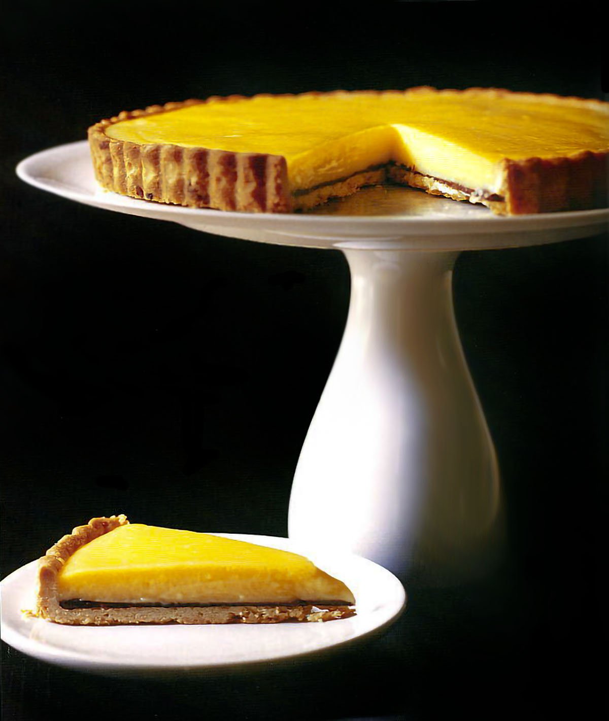 Meyer lemon tart on a white cake stand black background.