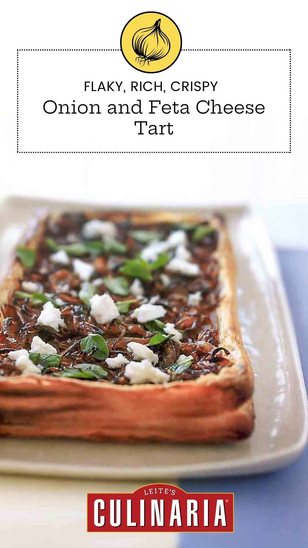 A whole puff pastry tart topped with caramelized onions, feta cheese, and oregano leaves on a rectangular platter.