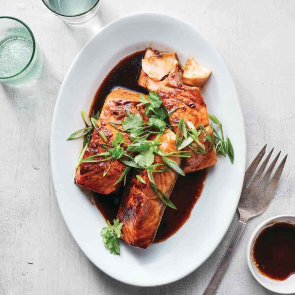 Three salmon filets on an oval platter in a soy caramel sauce, topped with cilantro and scallions.