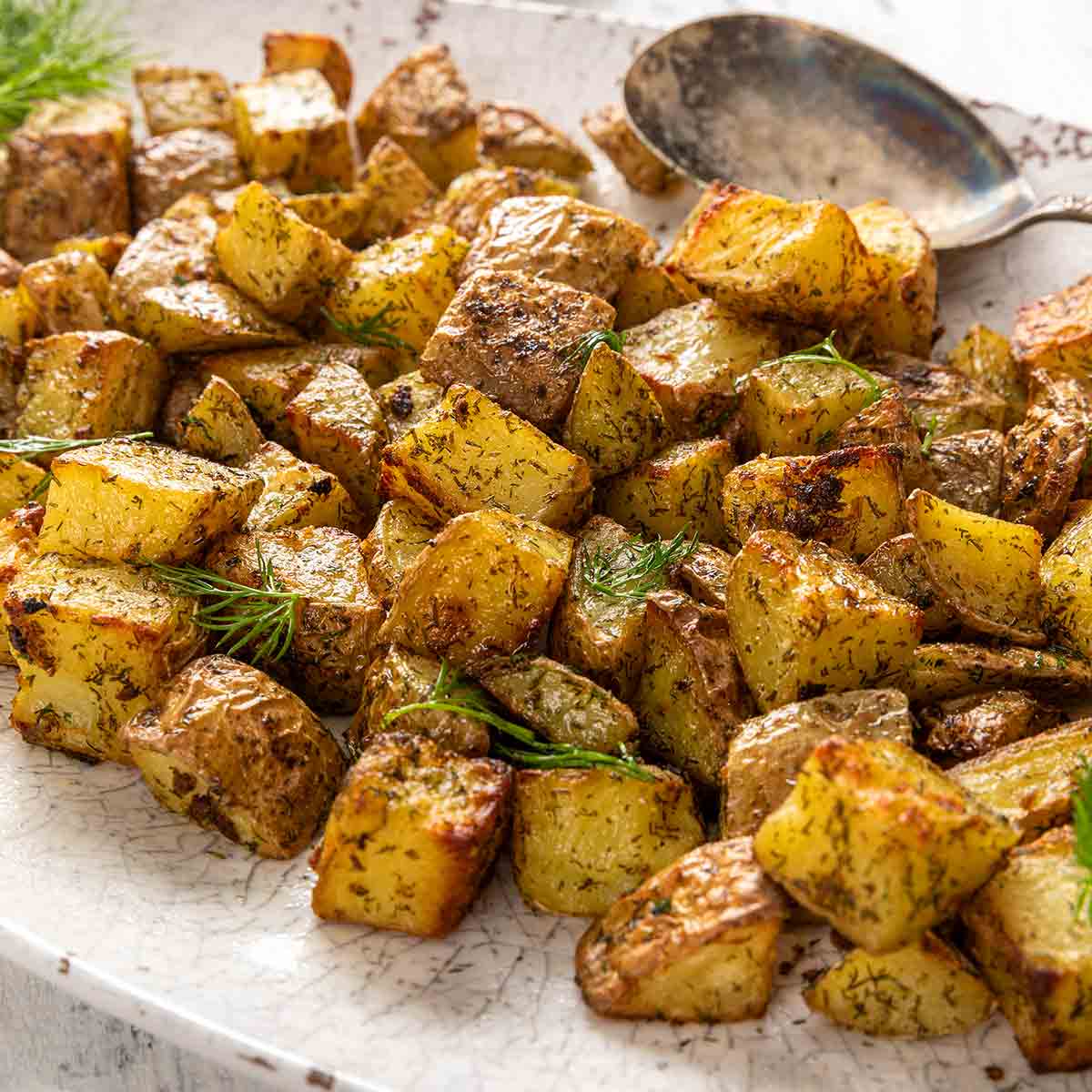 An oval platter filled with cubed roasted potatoes, garnished with fresh dill.