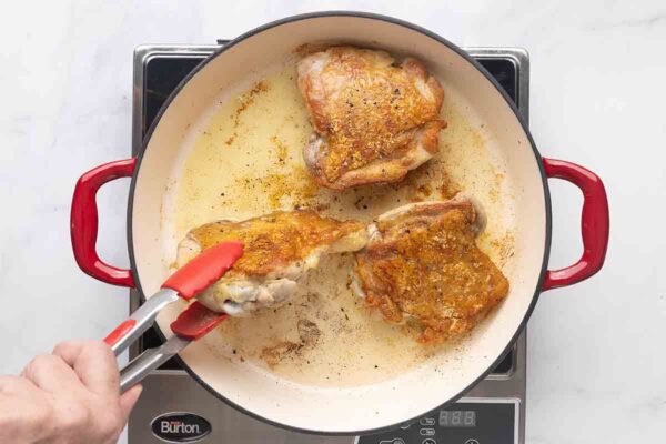 Three chicken thighs being seared in a skillet.
