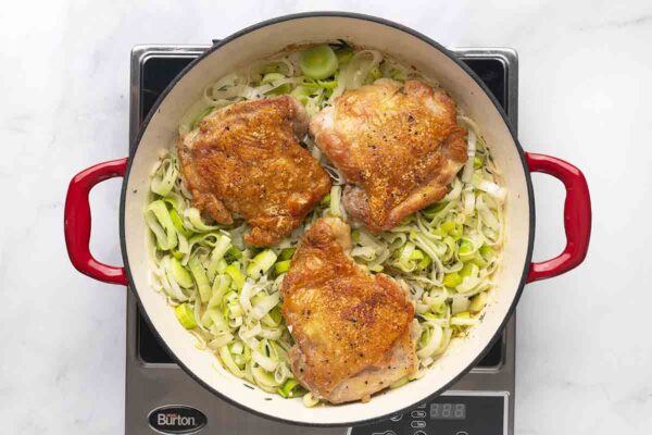 Three chicken thighs on top of a bed of leeks in a skillet.