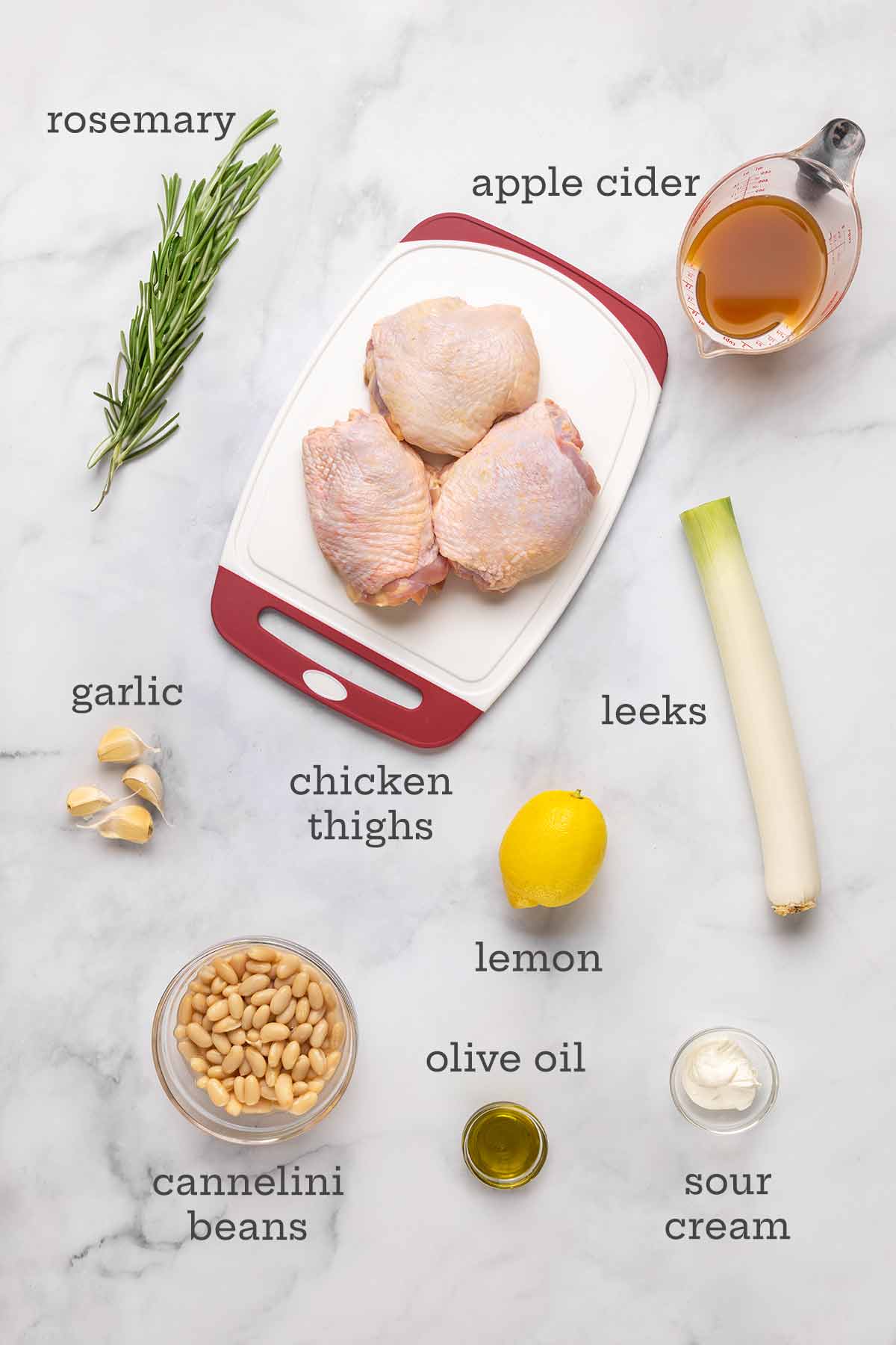 Ingredients for rosemary chicken--chicken thighs, rosemary, apple cider, garlic, leeks, lemon, beans, oil, and sour cream.