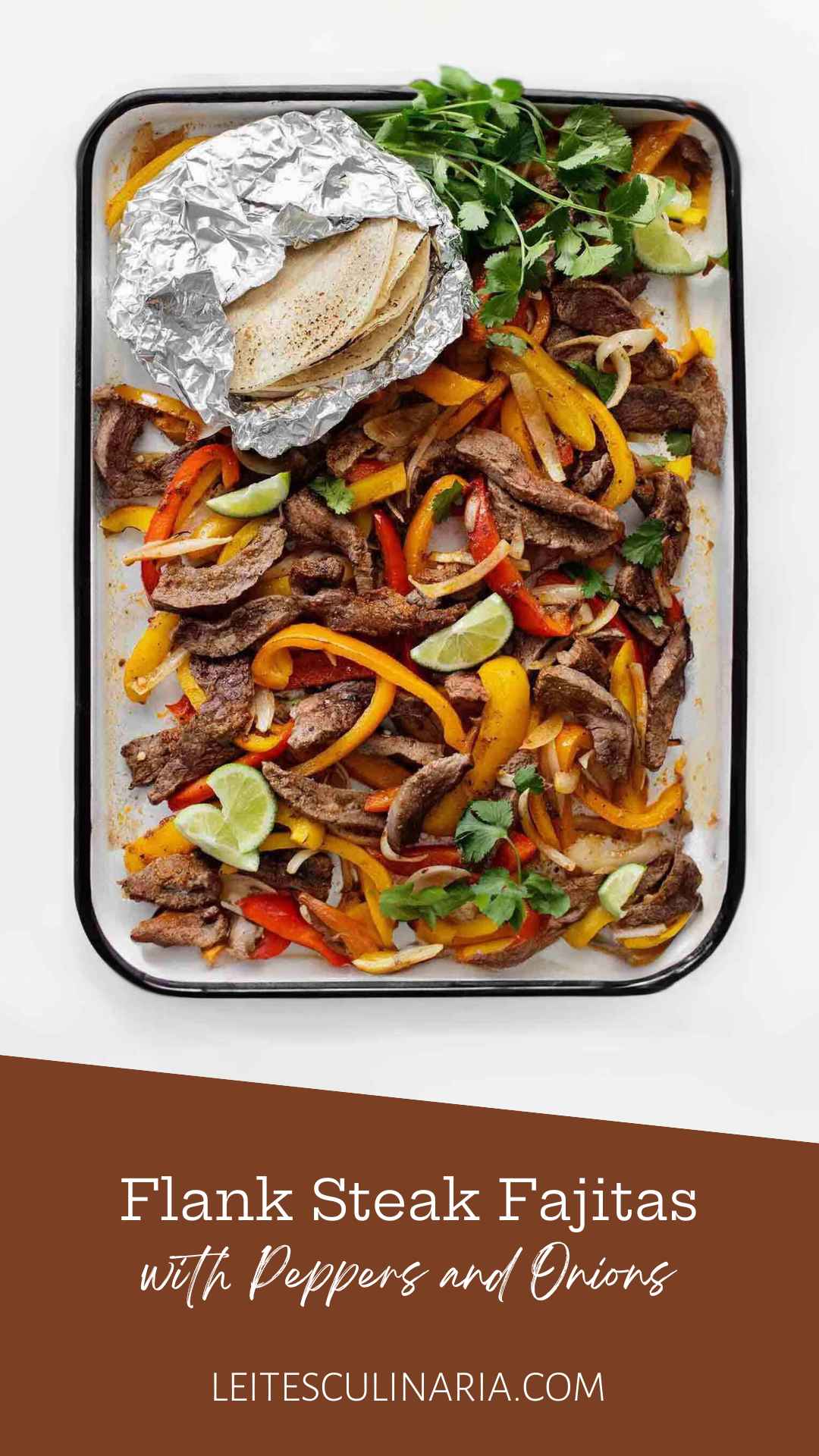 An enamel baking tray filled with sliced peppers, steak strips, onions, lime wedges, cilantro, and a foil packet of tortillas on the side.