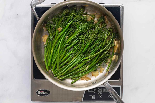 Broccolini and garlic slices in a metal skillet.
