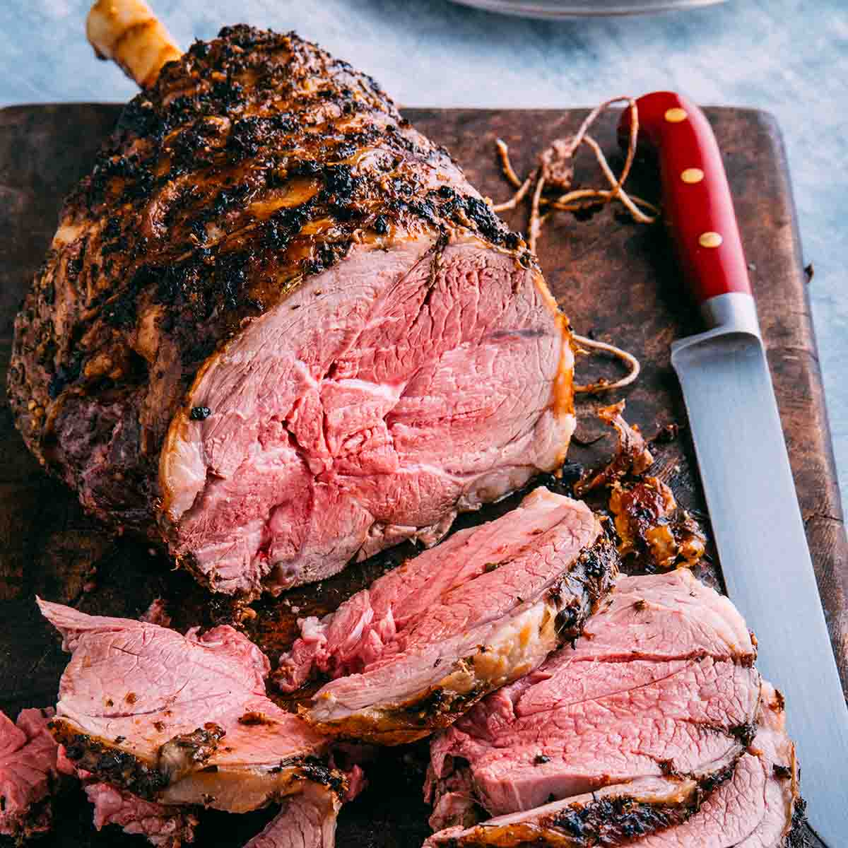A partially carved leg of lamb on a wooden cutting board.
