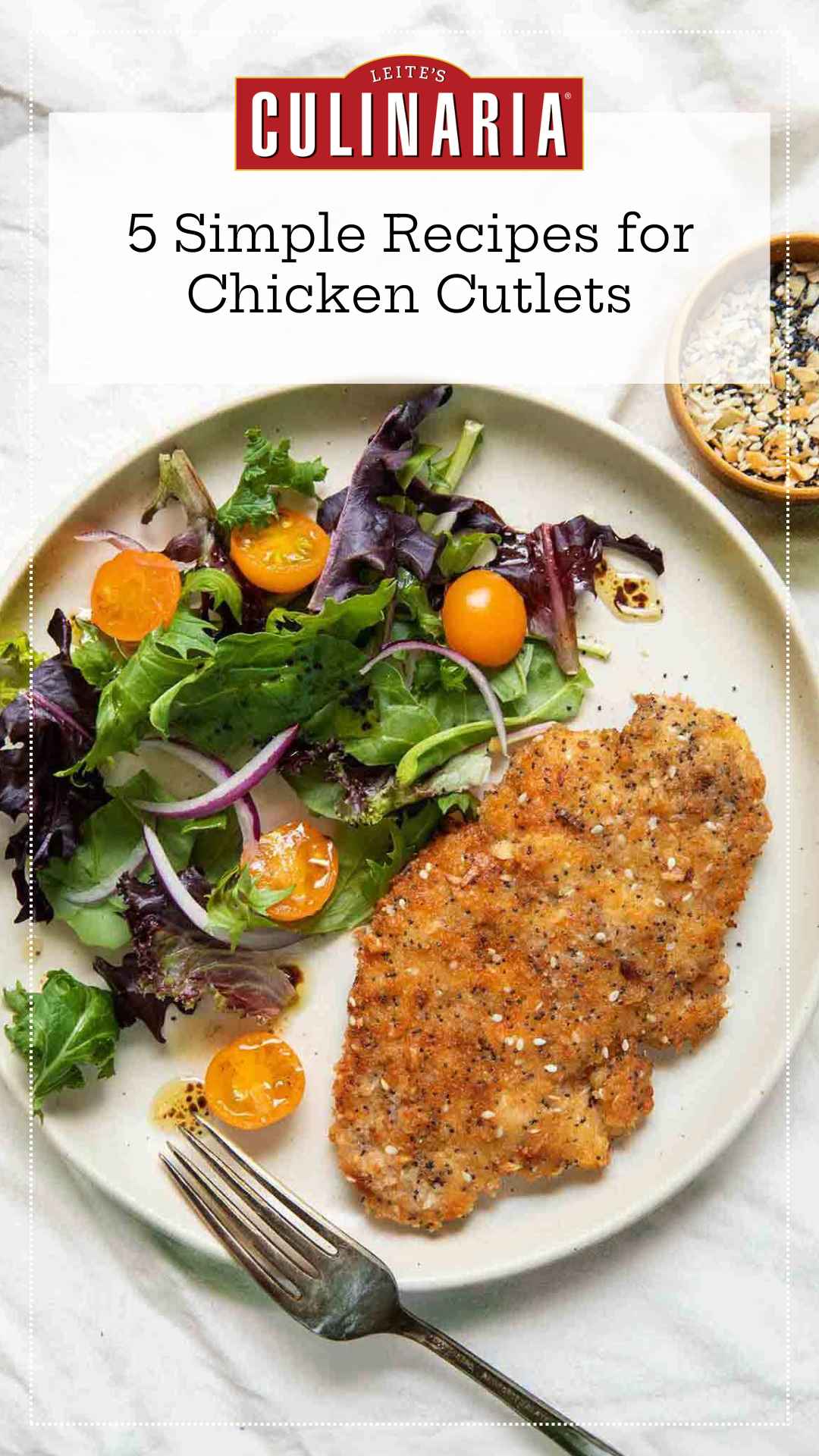 A breaded chicken cutlet on a plate with a salad of mixed greens, red onion, and cherry tomatoes.