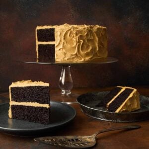 A chocolate caramel cake on a cake stand, with two slices cut from it on plates nearby.