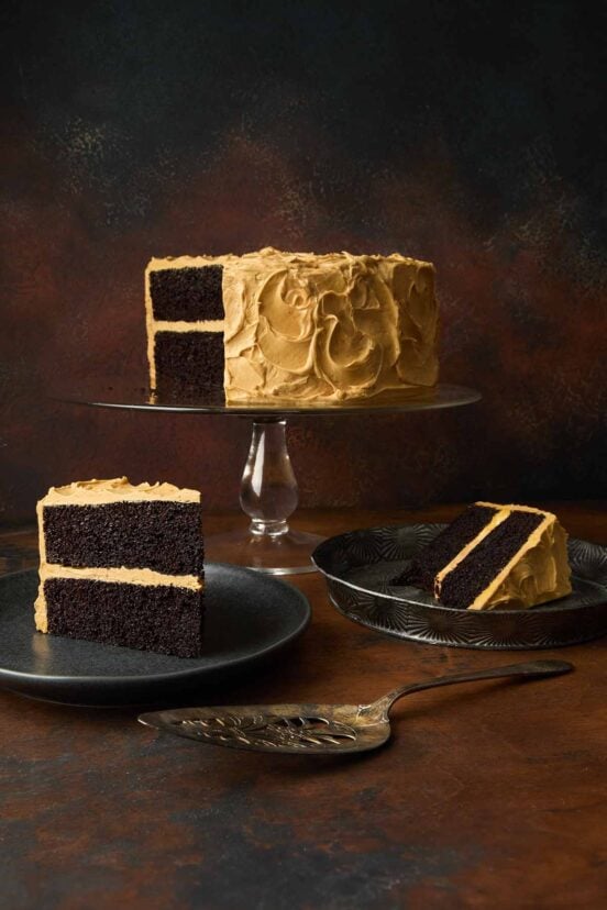 A chocolate caramel cake on a cake stand, with two slices cut from it on plates nearby.