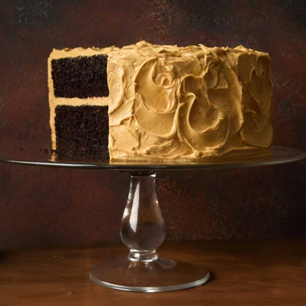 A chocolate caramel cake on a cake stand with a section cut from it.