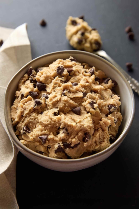 A bowl of edible chocolate chip cookie dough with a spoon and napkin on the side.