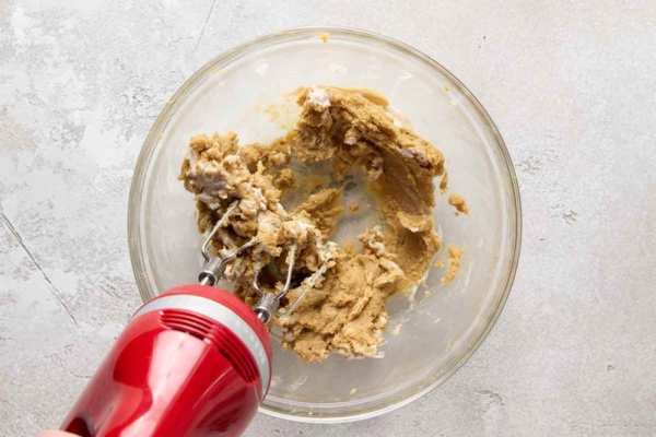 Cookie dough being mixed in a glass bowl with a hand mixer.