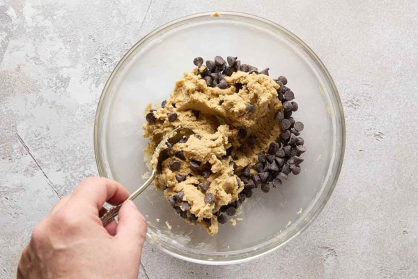 A person mixing chocolate chips into cookie dough.
