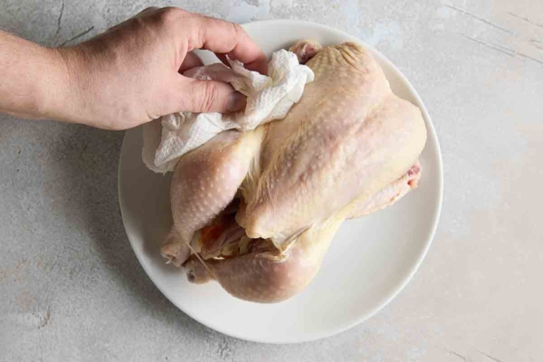 A person patting a whole chicken dry with paper towel.