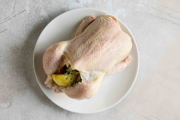 An uncooked whole chicken stuffed with herbs and lemon.
