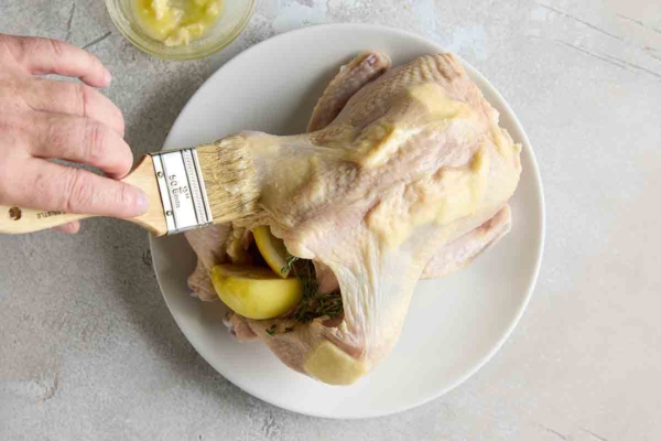A person brushing a stuffed chicken with melted butter.