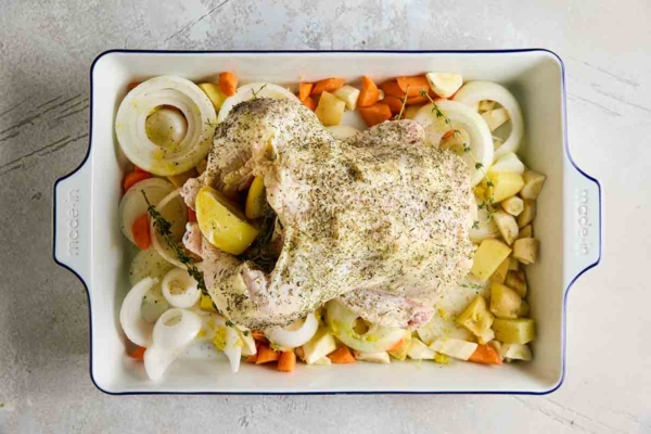 A stuffed chicken on a bed of root vegetables and onion slices.