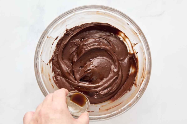 Vanilla being added to a bowl of chocolate frosting.