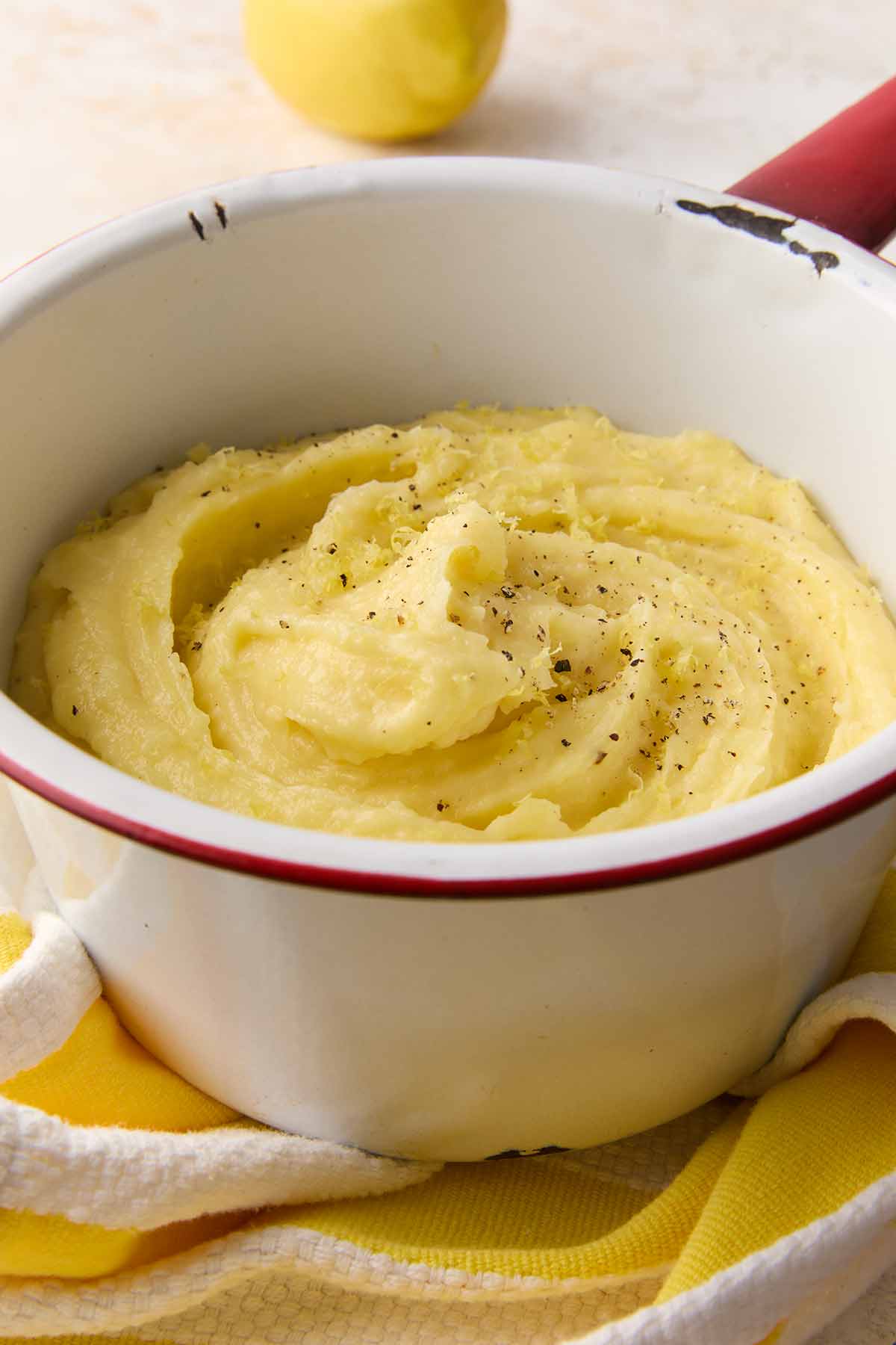 An enamel bowl filled with mashed potatoes, topped with black pepper and lemon zest.