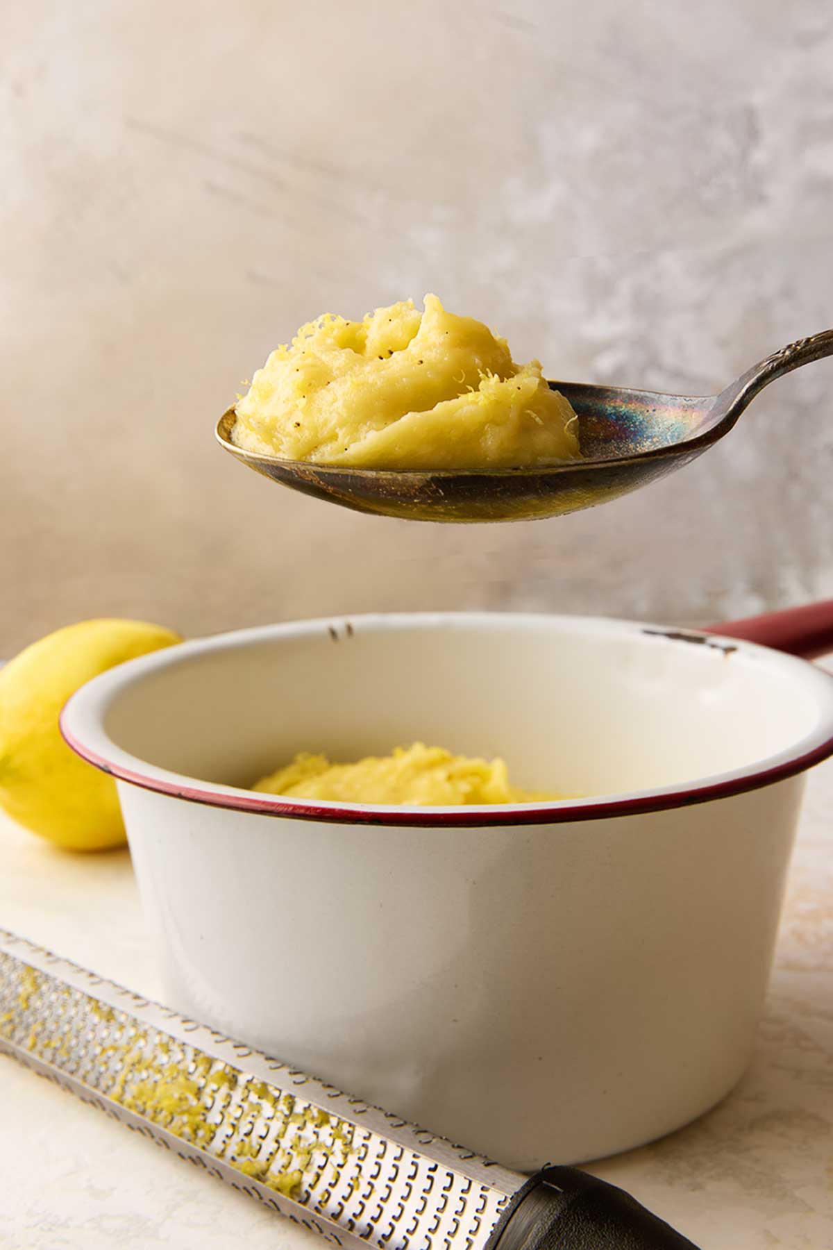 A spoonful of mashed potatoes with lemon being held over a bowl of mashed potatoes.