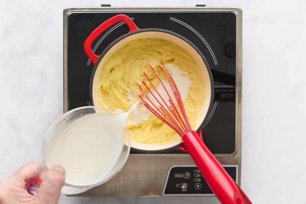 A person adding milk to a saucepan of mashed potatoes.