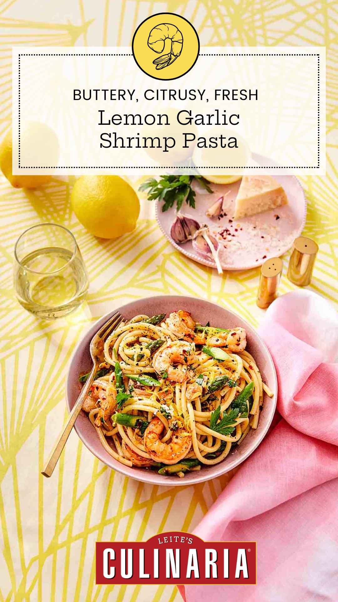 A bowl filled with lemon garlic shrimp pasta with a glass of white wine, a pink napkin, and lemons nearby.