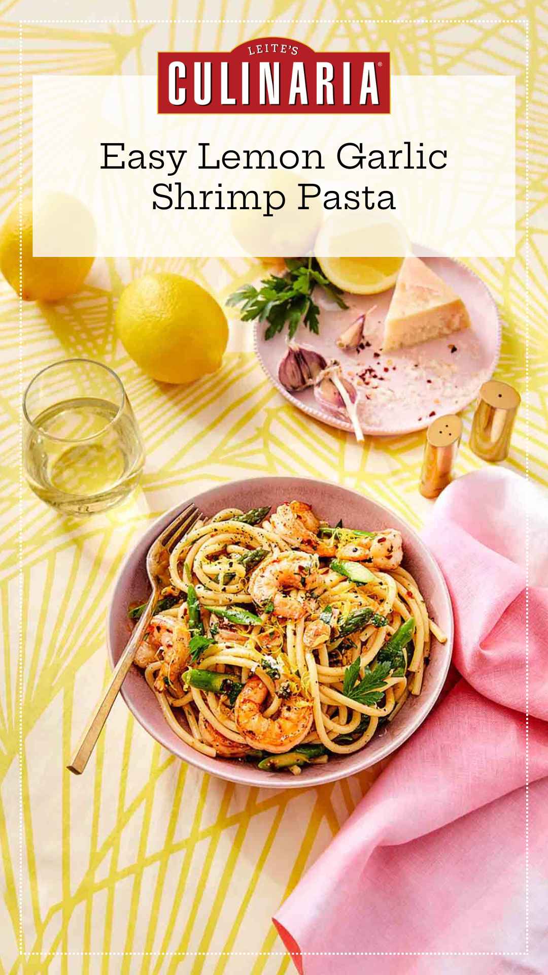 A bowl filled with lemon garlic shrimp pasta with a glass of white wine, a pink napkin, and lemons nearby.