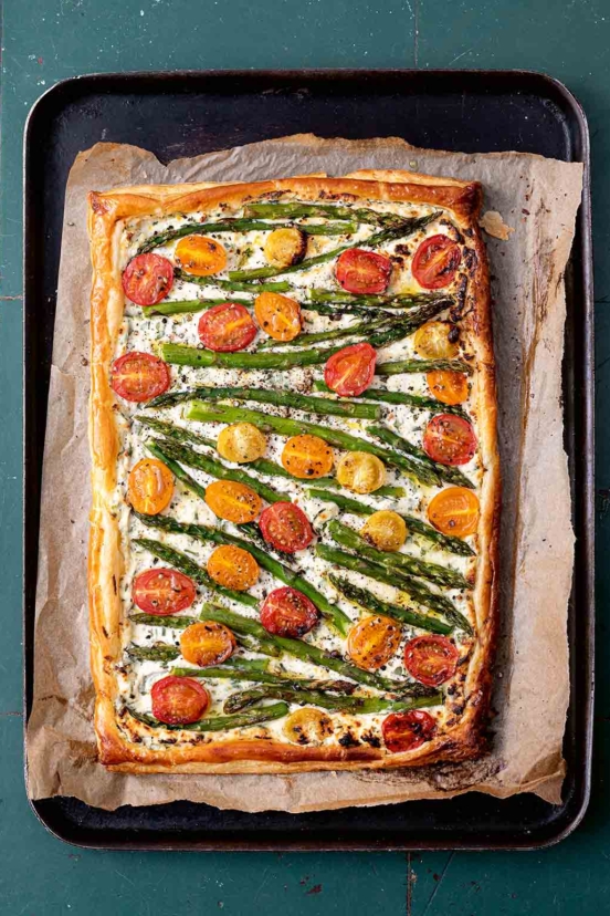 A puff pastry tart topped with ricotta, cherry tomatoes, and asparagus.