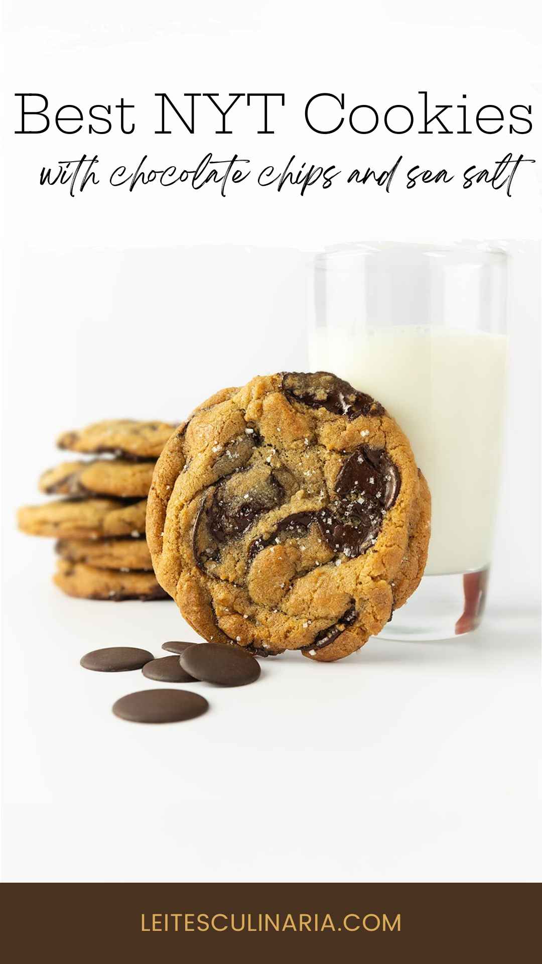 A chocolate chip cookie leaning against a glass of milk with several more stacked in the background.