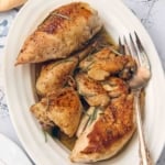 Pieces of browned chicken topped with garlic and rosemary leaves on a white oval platter.