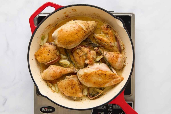 Pieces of browned chicken in a skillet with garlic and rosemary.