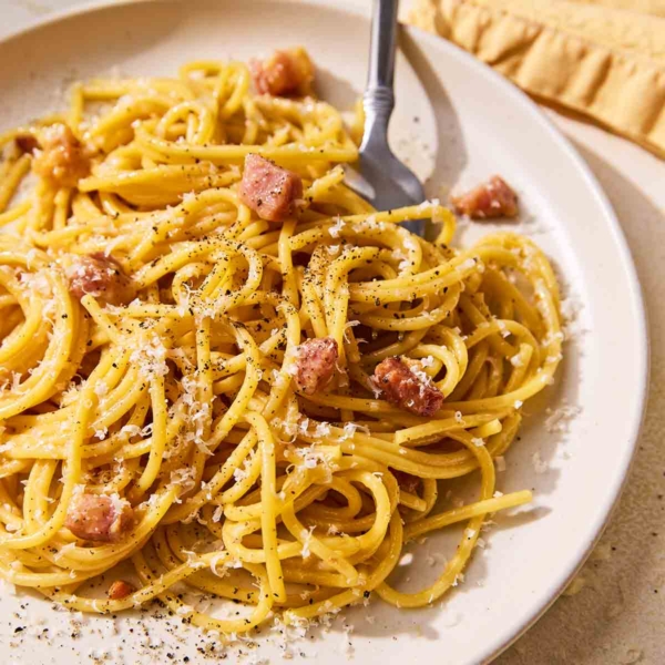 A plate of spaghetti carbonara with crispy pancetta, Parmesan, and ground black pepper.