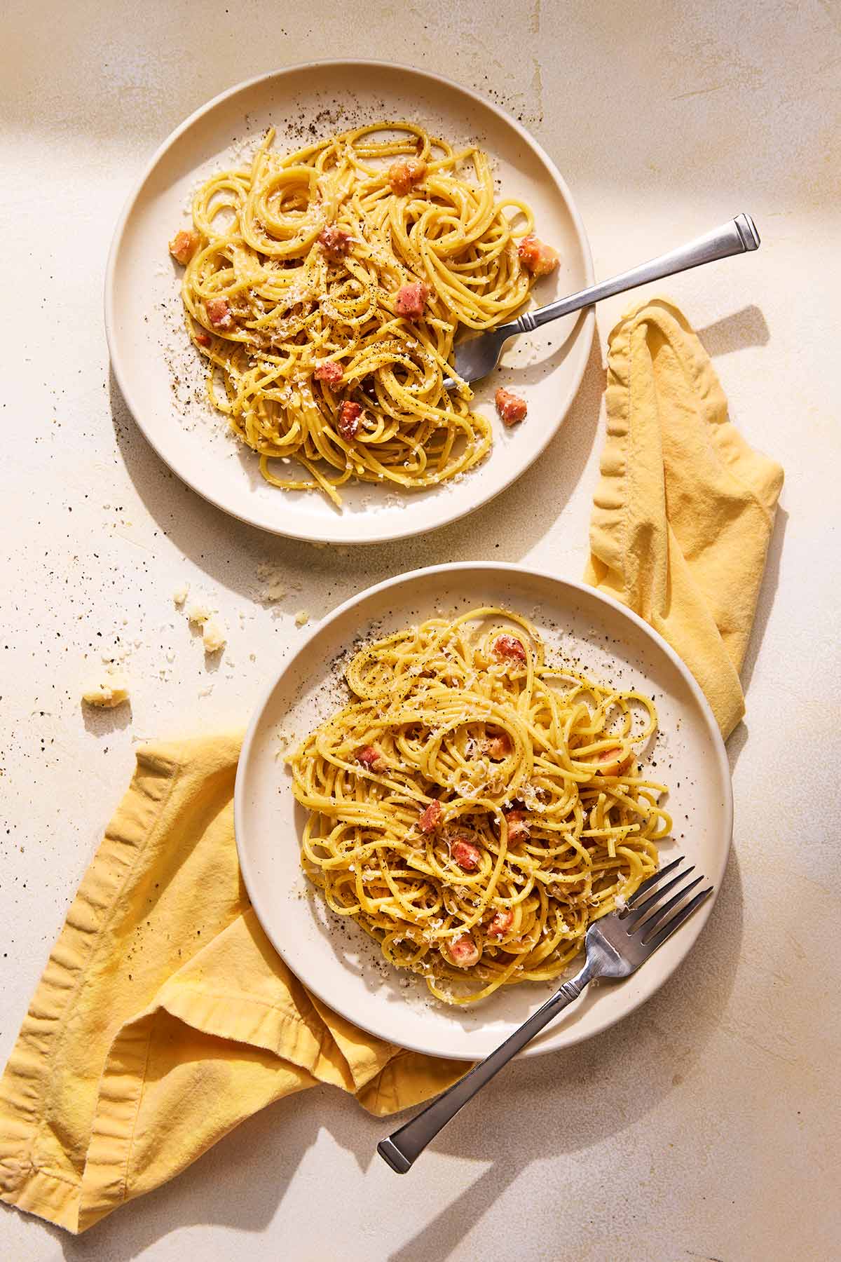 Two plates of spaghetti alla carbonara with cubed guanciale.