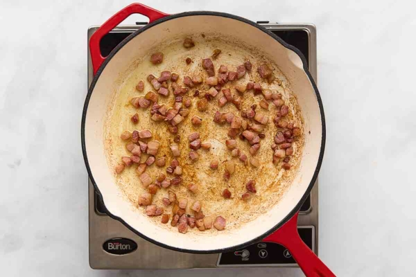 Cubes of pancetta frying in a skillet.