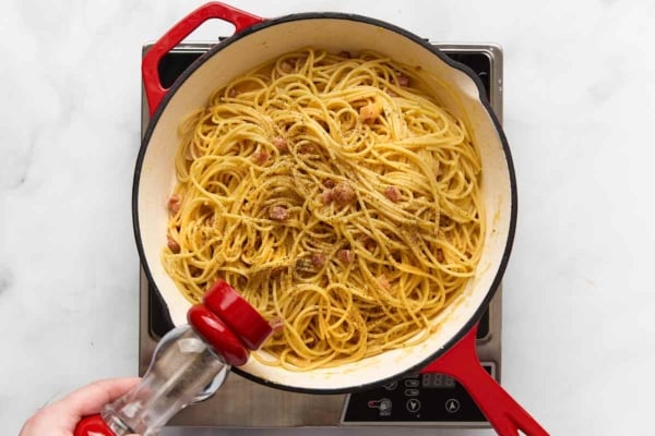 A person grinding pepper into a skillet of spaghetti carbonara.