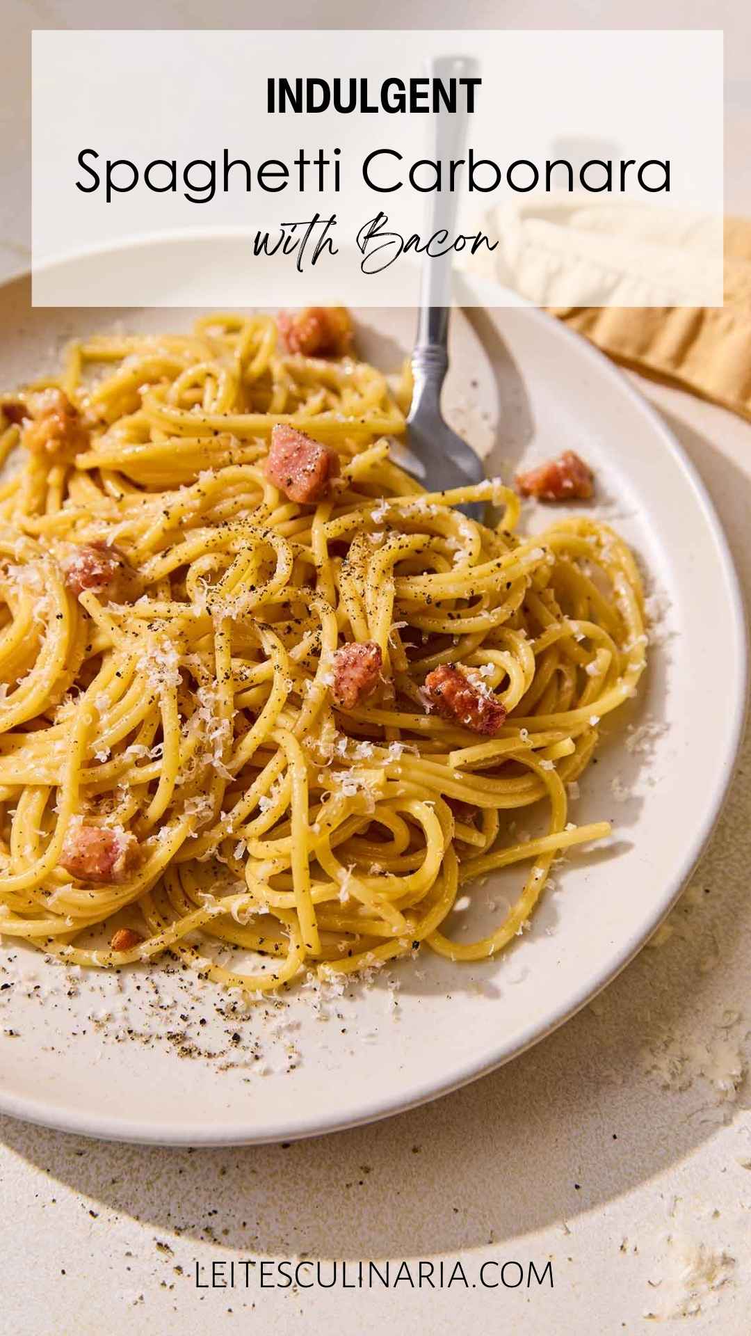 A plate of spaghetti carbonara with cubes of pancetta, Parmesan, and black pepper.