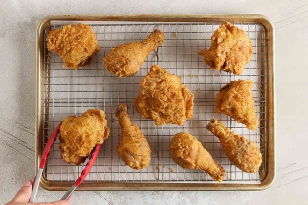 Pieces of crispy fried chicken cooling on a wire rack set over a baking sheet.