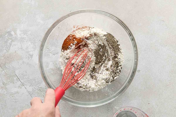 A person whisking a bowl of flour and spices to create batter for fried chicken.