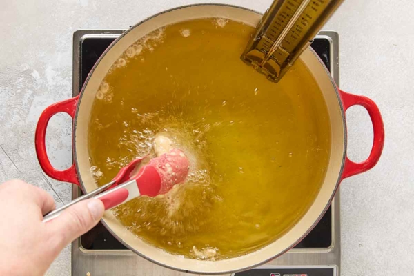 A piece of chicken being added to a pot of bubbling oil.
