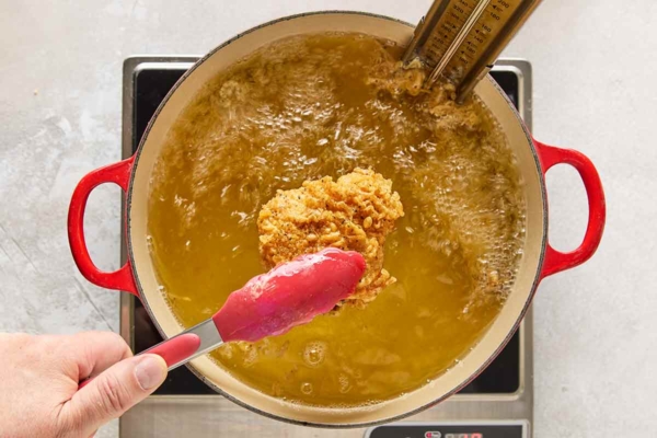 A piece of crispy fried chicken being lifted from a pot of bubbling oil.